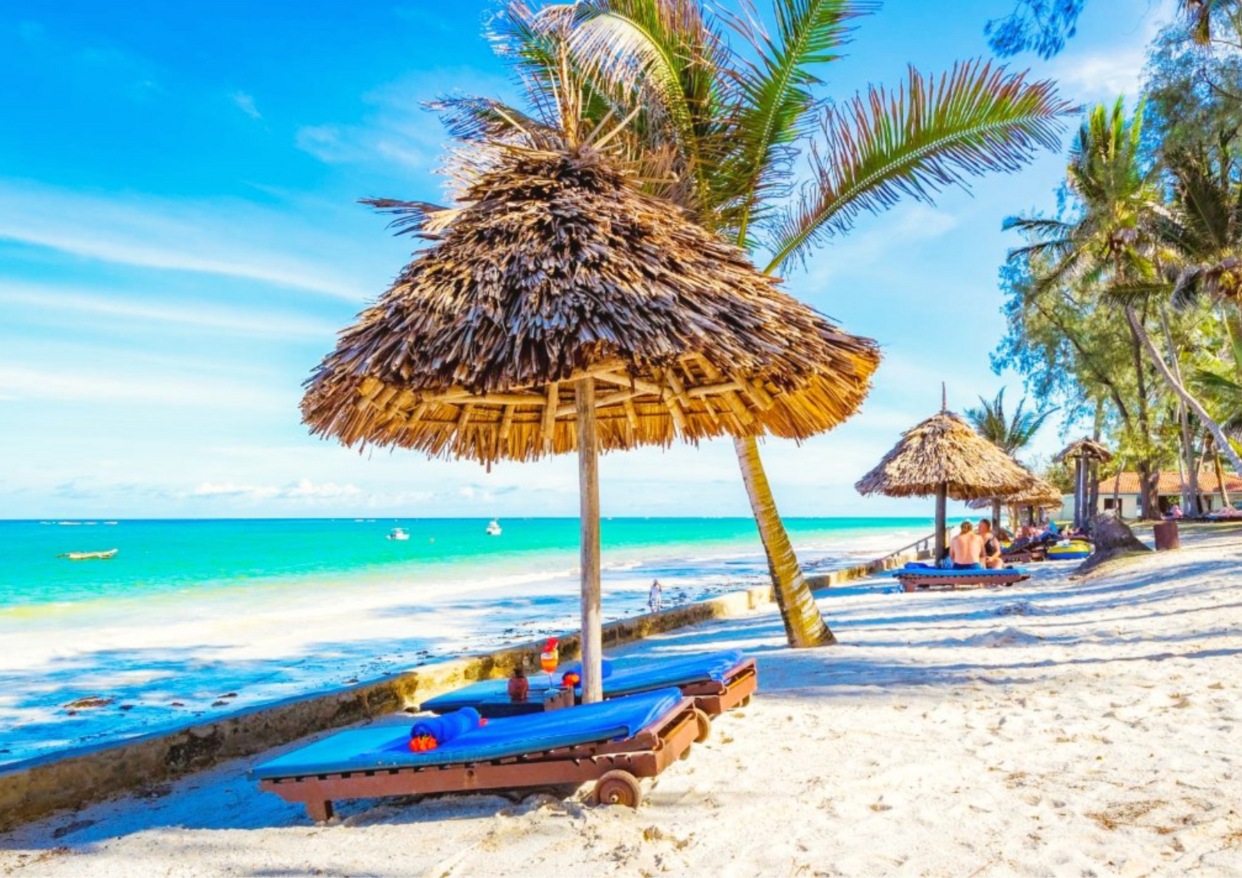 Beach scene with thatched umbrellas, lounge chairs, and turquoise ocean, perfect for enjoying Kirenge Gold premium Kenyan coffee while relaxing by the seaside