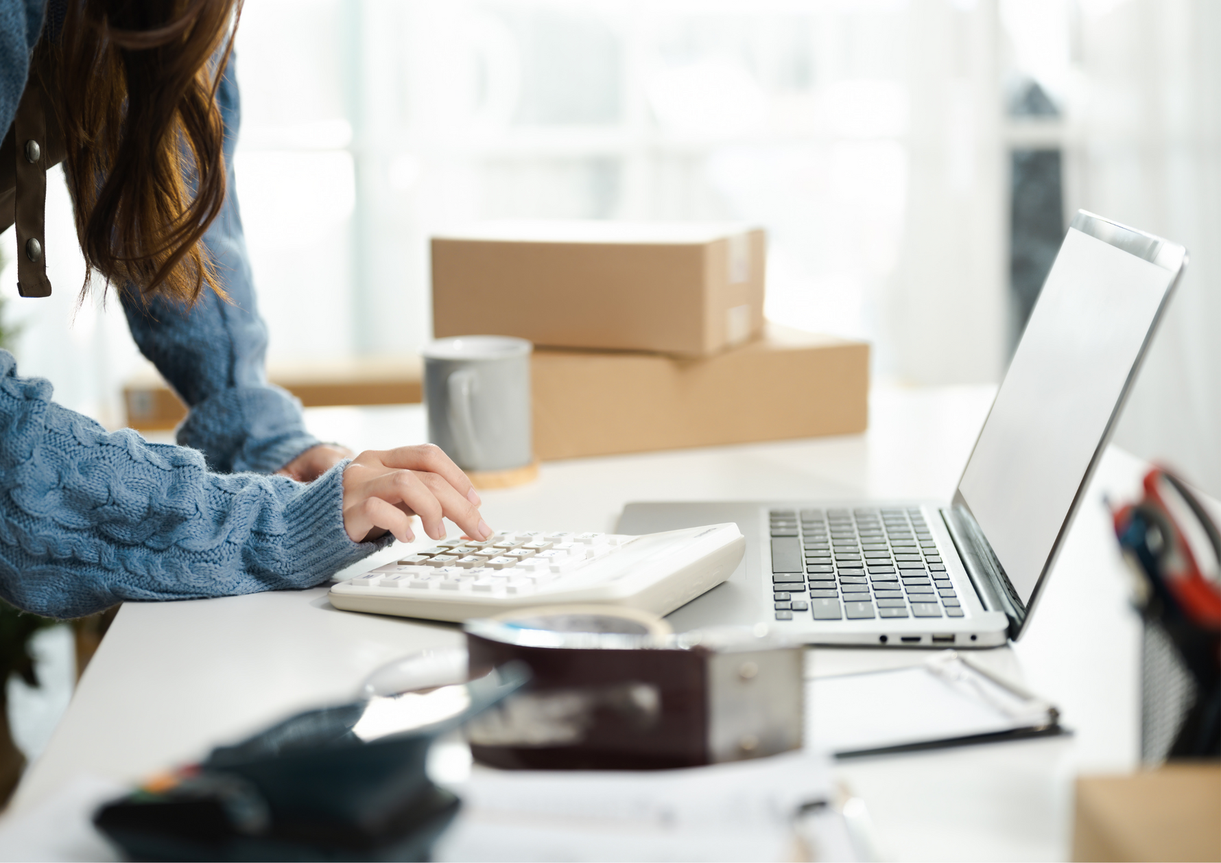 Person typing on a laptop at a desk with boxes in the background, managing Kirenge Gold premium Kenyan coffee orders and inventory.