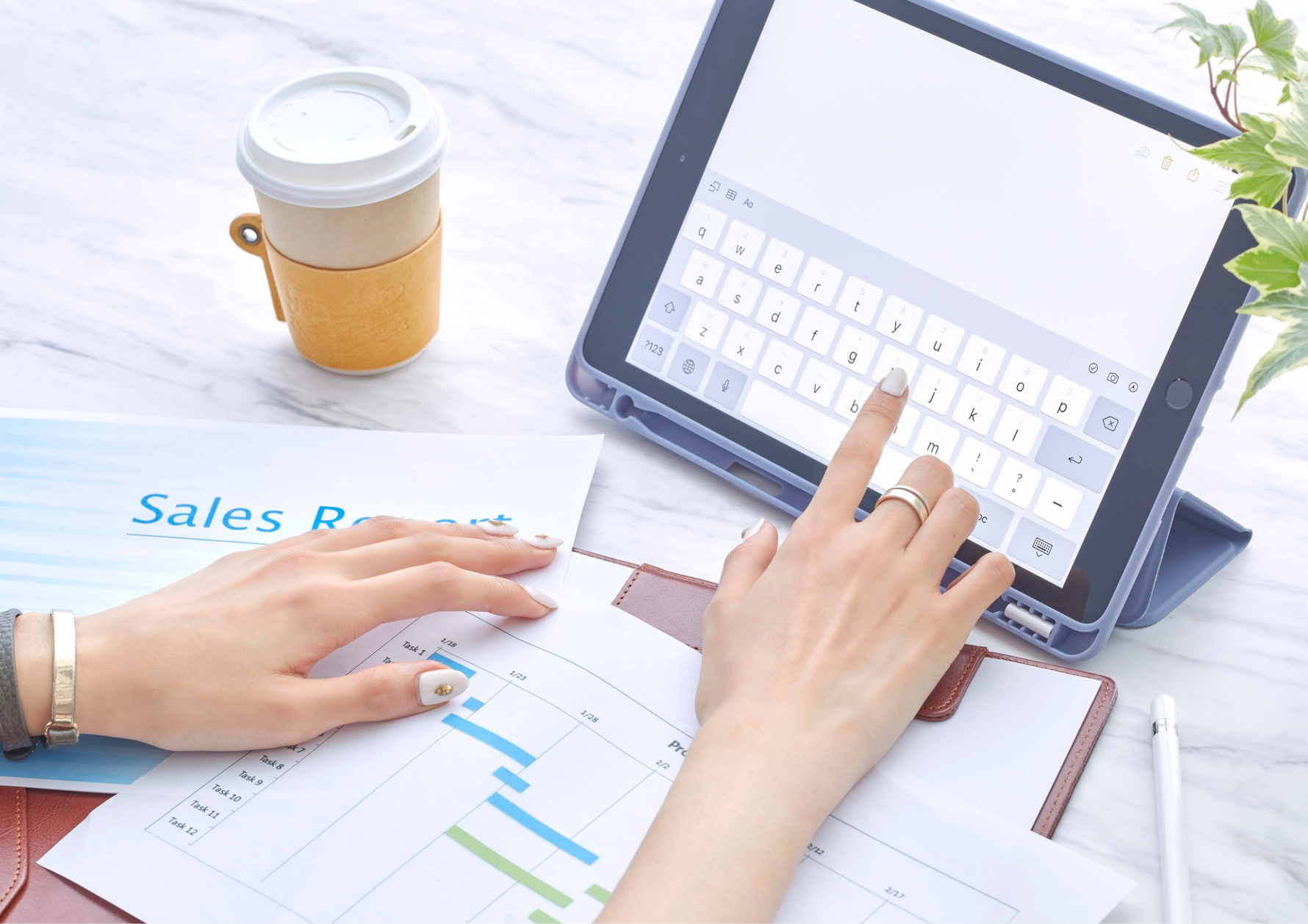 Person using a tablet with a keyboard on a desk alongside a cup of Kirenge Gold Kenyan premium coffee and documents, illustrating a productive coffee-fueled workspace.