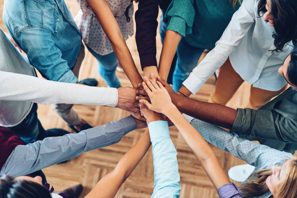 Group of people with their hands stacked together in a circle, symbolizing teamwork and community, aligned with Kirenge Gold’s coffee farm and business partnerships.
